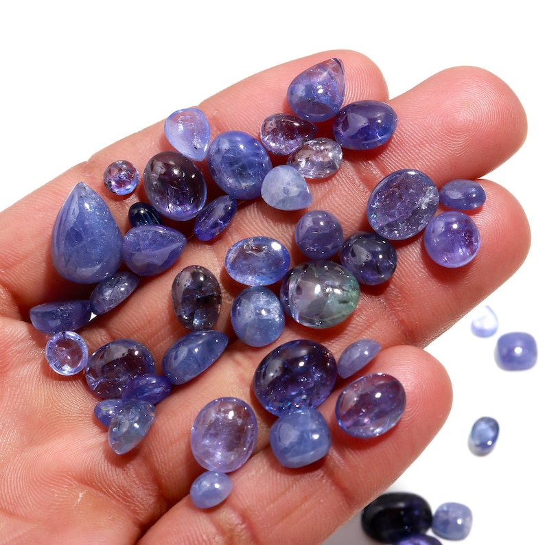 May include: A collection of loose, faceted, blue gemstones. The gemstones are various shades of blue and have a variety of shapes and sizes. The gemstones are displayed on a hand.