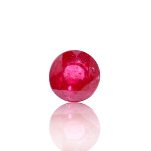 May include: A round, red gemstone with a faceted cut. The gemstone is reflecting light, creating a sparkle effect.