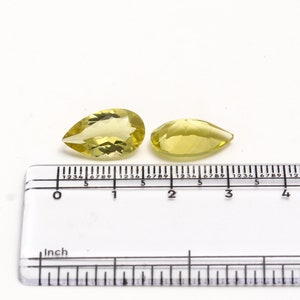 Może przedstawiać: Dwa żółte kamienie szlachetne w kształcie gruszki, o długości około 2,5 cm, są pokazane na linijce.