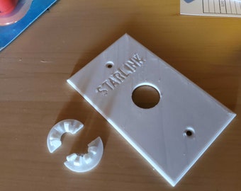May include: A white plastic wall plate with the word "STARLINK" printed on it. The plate has a round hole in the centre and a small hole in the bottom right corner.