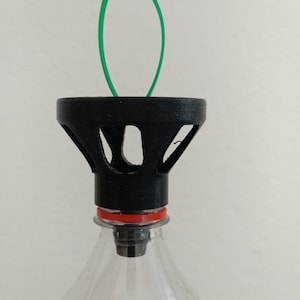 以下が含まれることがあります： 緑色の結束バンドが付いた黒いプラスチック製のボトルトップ。ボトルトップは、縁に一連の穴が開いた漏斗型の開口部があります。ボトルトップは透明なプラスチックボトルに取り付けられています。