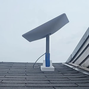 Könnte beinhalten: Eine weiße Satellitenschüssel, die auf einem Dach mit einem blauen und weißen Ständer montiert ist. Die Antenne ist auf den Himmel gerichtet.