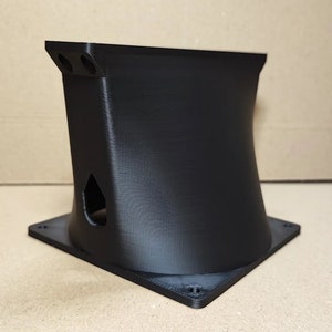 Op de afbeelding: Een zwart, 3D-geprint object met een vierkante basis en een gebogen, uitlopend lichaam. De bovenkant heeft twee cirkelvormige openingen en de zijkant heeft een druppelvormige uitsparing. Het object lijkt van plastic te zijn.