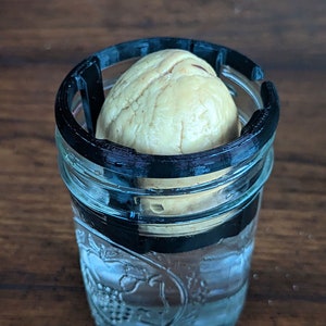 Può includere: Un seme di avocado bianco è posto all'interno di un barattolo di vetro trasparente con un anello nero stampato in 3D attorno alla parte superiore.