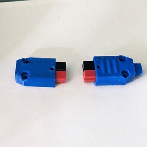 Könnte beinhalten: Zwei blaue Kunststoffstecker mit roten und schwarzen Drähten. Die Stecker haben eine strukturierte Oberfläche und sind so konzipiert, dass sie miteinander verbunden werden können.