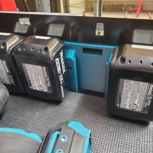 May include: Three black Makita 18V 4.0Ah lithium-ion batteries are stored in a blue and black battery holder. The batteries are labelled with the Makita logo and model number.