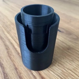 May include: A black 3D printed cylindrical container with a smaller cylindrical opening at the top. The container has a cut-out on the side.