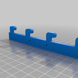 May include: A blue plastic bracket with three hook-shaped protrusions. The bracket has two small holes and is designed for mounting or hanging items. The object is rendered on a grid background.