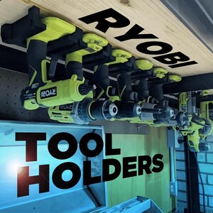 Könnte beinhalten: Ein Satz schwarzer und gelber Elektrowerkzeuge ist an einem Holzregal mit dem Wort "RYOBI" angebracht. Die Werkzeuge hängen an schwarzen Werkzeugträgern. Der Text "TOOL HOLDERS" ist auf einer blauen Fläche unter dem Regal aufgedruckt.