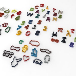 May include: A set of colourful cookie cutters in various shapes, including letters, numbers, symbols, and holiday-themed designs. The cutters are made of metal and are arranged on a white surface.