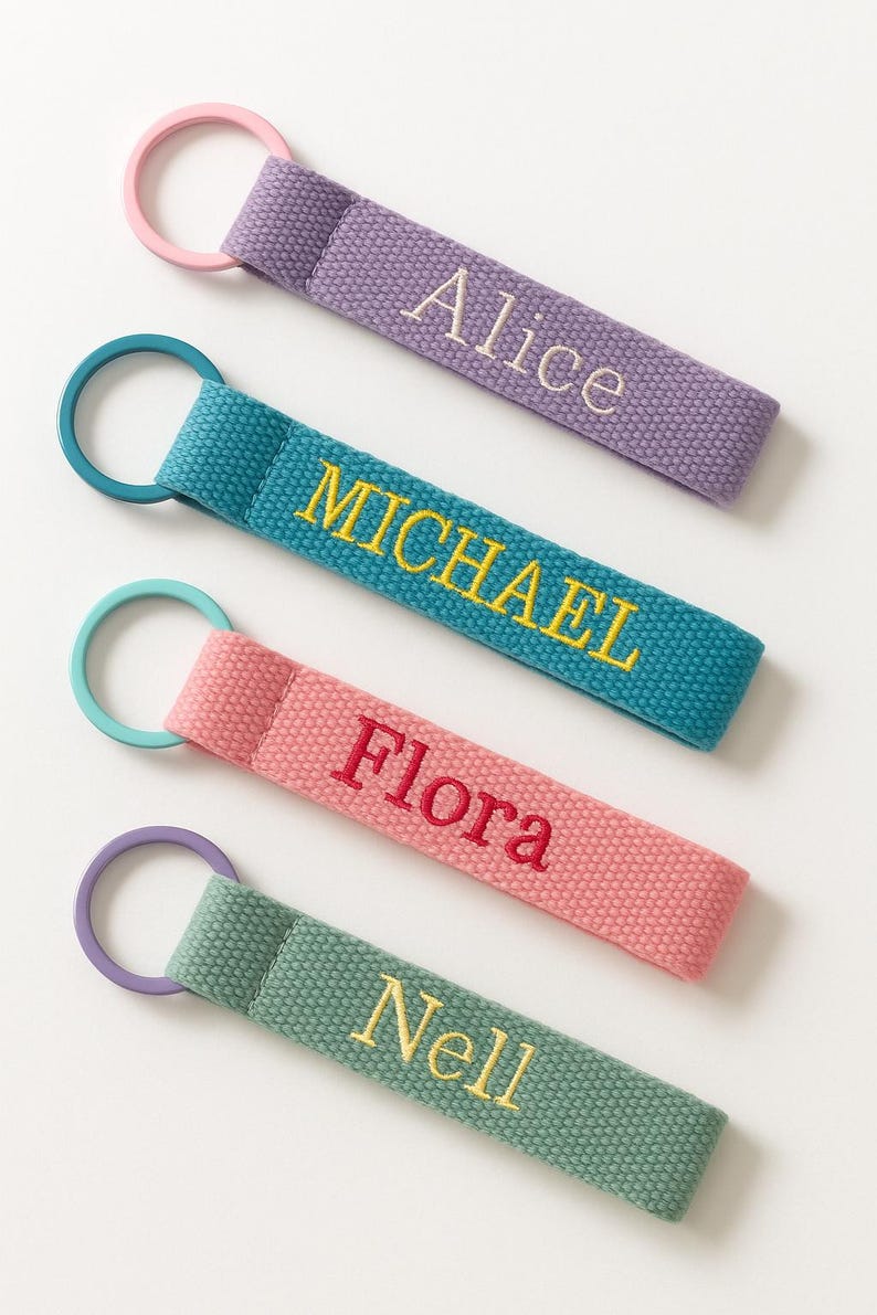 May include: Four personalized keychains in various colors: purple with "Alice", teal with "MICHAEL", pink with "Flora", and green with "Nell". Each keychain features a matching ring.