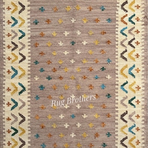 May include: Rectangular area rug with a central field of taupe, adorned with small, scattered floral motifs in yellow, teal, and brown. The border features a cream-colored band with geometric patterns in teal, brown, and yellow. The rug has a fringed edge and the text "Rug Brothers".