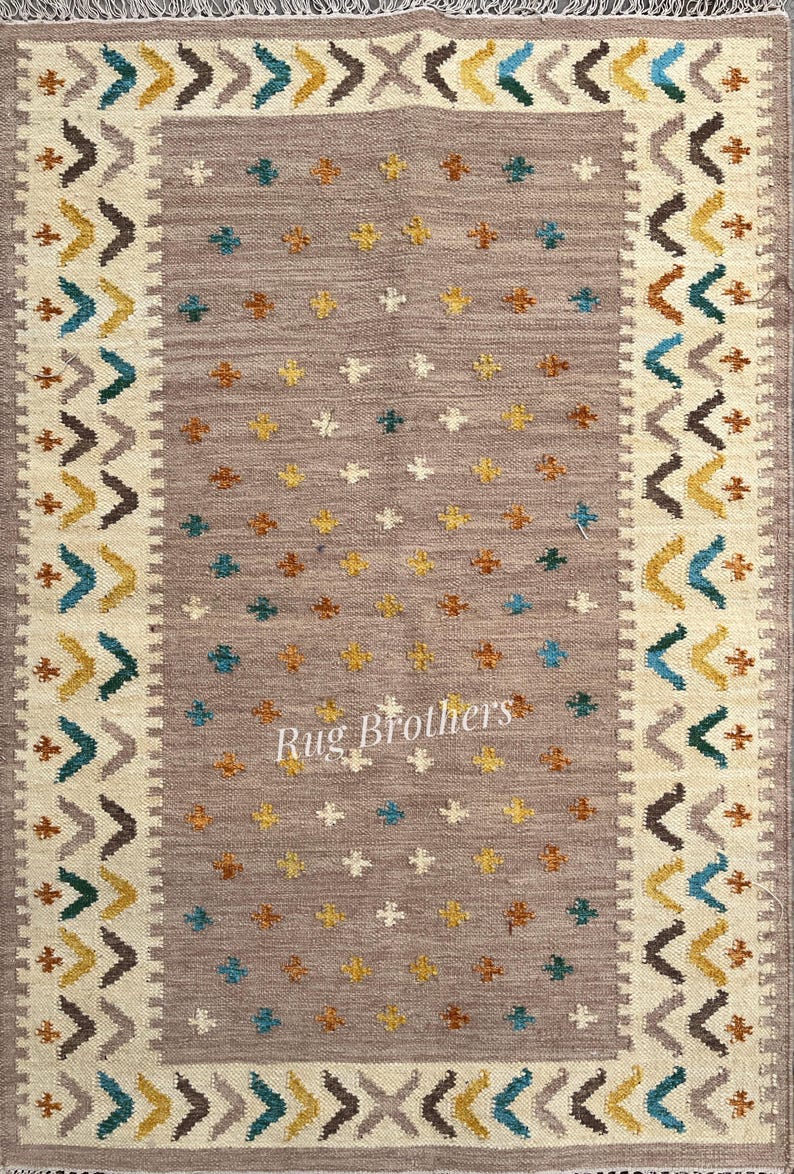 May include: Rectangular area rug with a central field of taupe, adorned with small, scattered floral motifs in yellow, teal, and brown. The border features a cream-colored band with geometric patterns in teal, brown, and yellow. The rug has a fringed edge and the text "Rug Brothers".