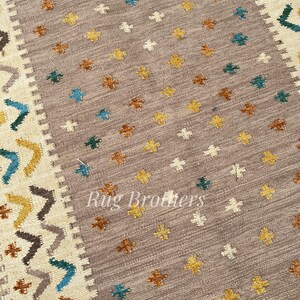 May include: A rectangular area rug with a central field of taupe, adorned with small, repeating floral patterns in yellow, brown, white, and teal. The border features geometric designs in similar colors. The text "Rug Brothers" is visible.