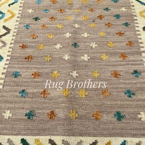 May include: A rectangular rug with a central field of taupe, adorned with small, colorful floral patterns in yellow, teal, and brown. The border features geometric designs in cream, brown, teal, and yellow. The text "Rug Brothers" is in the center.