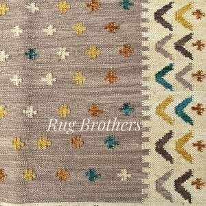 May include: Close-up of a woven rug with a neutral gray background. The rug features a pattern of small, colorful floral motifs in yellow, teal, and brown. The border has a geometric design with chevron and cross patterns. The text "Rug Brothers" is visible.