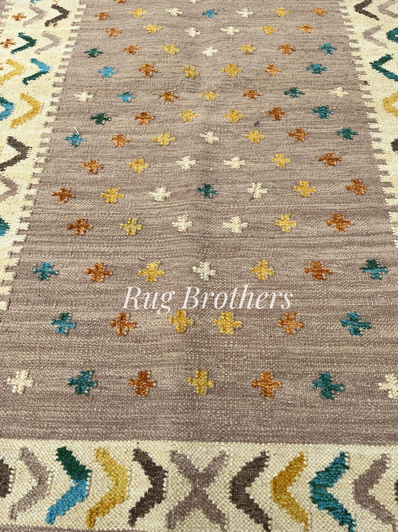 May include: A rectangular rug with a central field of taupe, adorned with small, colorful floral patterns in yellow, teal, and brown. The border features geometric designs in cream, brown, teal, and yellow. The text "Rug Brothers" is in the center.