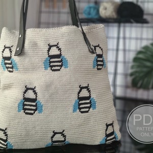 May include: A white crocheted tote bag with a black and blue bee pattern. The bag has leather straps and the text "PDF PATTERN ONLY" is visible in the lower right corner.