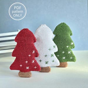 Può includere: Tre alberi di Natale all'uncinetto in rosso, bianco e verde. Ogni albero ha una base marrone ed è decorato con accenti bianchi o verdi a forma di croce e stella. Il testo "PDF pattern ONLY" è in un cerchio in alto a sinistra.