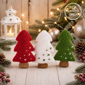 Può includere: Tre ornamenti per albero di Natale all'uncinetto in rosso, bianco e verde, ciascuno con una base marrone e dettagli a stella ricamati. L'albero rosso ha stelle bianche, quello bianco ha stelle verdi e quello verde ha stelle bianche. Il testo recita PDF pattern ONLY.