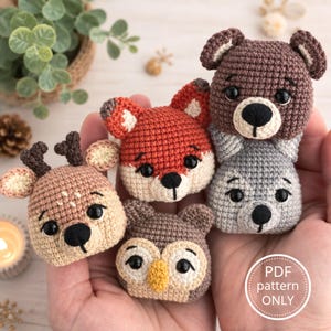 Può includere: Cinque piccole teste di animali all'uncinetto che includono un cervo, una volpe, un orso, un gufo e un lupo. Ogni figura presenta occhi in plastica nera e un naso ricamato. Un grafico circolare bianco contiene il testo PDF pattern ONLY.