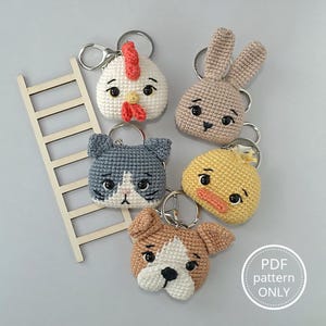 Puede incluir: Una colección de llaveros de animales hechos a mano con ganchillo, que incluyen un pollo, un conejo, un gato, un pato y un perro. Cada llavero presenta una cara de animal detallada con rasgos expresivos y un anillo de metal. Los llaveros son de varios colores y texturas.