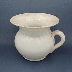 May include: White ceramic chamber pot with a wide, flat rim and a single handle. The pot has a rounded body and a slightly flared base.