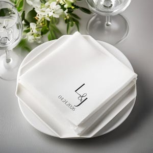 White cocktail napkins stacked on a plate with monogram and date.