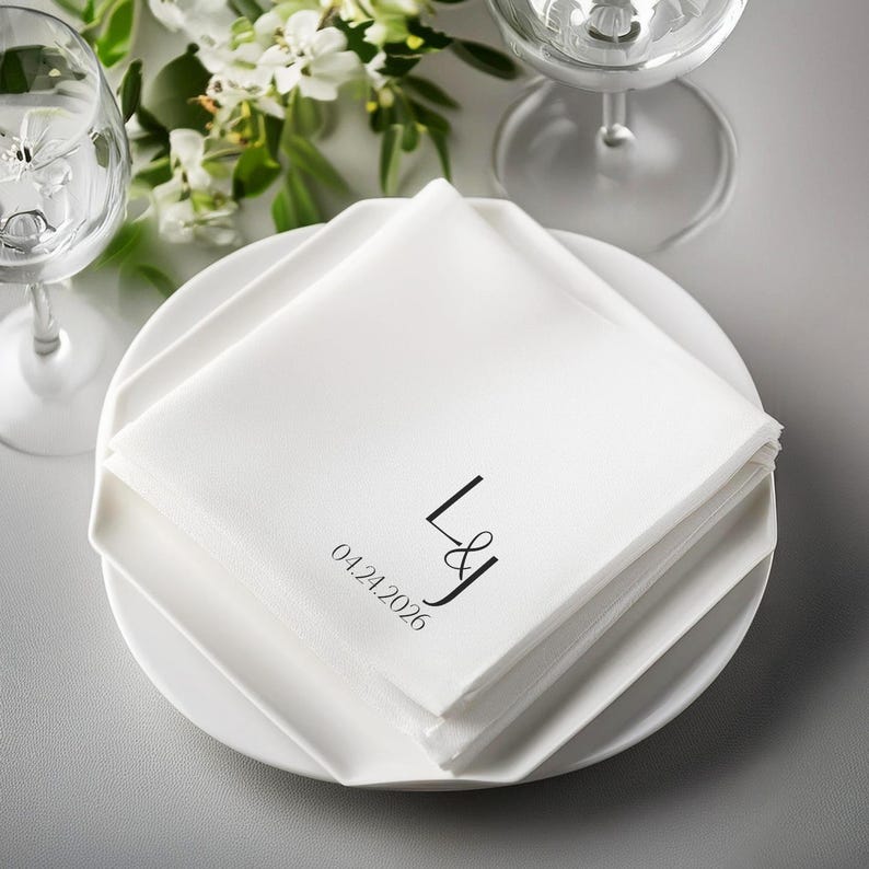 White cocktail napkins stacked on a plate with monogram and date.
