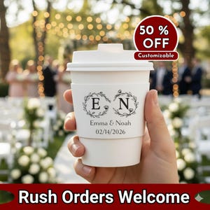 Pode incluir: Copo de café de papel branco com tampa e manga personalizada. A manga apresenta as iniciais "E" e "N" dentro de coroas de louro, com os nomes "Emma & Noah" e a data "02/14/2026" impressos abaixo. Um círculo vermelho indica "50% OFF" e "Personalizável".
