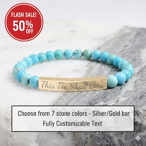 Puede incluir: Una pulsera de cuentas turquesas con una barra dorada grabada con las palabras "This Too Shall Pass". La imagen también incluye un círculo rojo con el texto "FLASH SALE! 50% OFF". El texto debajo de la pulsera dice "Choose from 7 stone colors - Silver/Gold bar Fully Customizable Text."