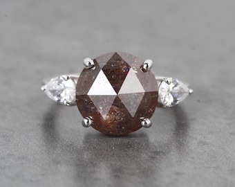 Può includere: Un anello d'argento con un grande diamante marrone sfaccettato al centro e due diamanti più piccoli a forma di pera su entrambi i lati.