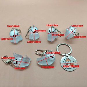 May include: A collection of Halloween-themed keychains featuring translucent ghost designs with black facial features. The keychains vary in size, with the largest measuring 1.3 inches wide. One keychain has a circular tag with a pumpkin and the text "You're my Boo."