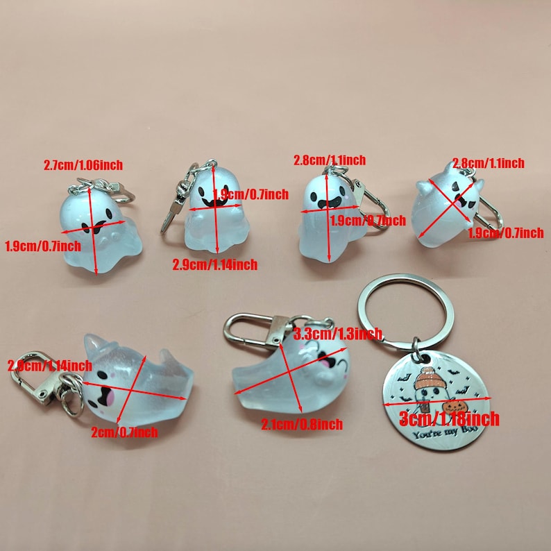 May include: A collection of Halloween-themed keychains featuring translucent ghost designs with black facial features. The keychains vary in size, with the largest measuring 1.3 inches wide. One keychain has a circular tag with a pumpkin and the text "You're my Boo."