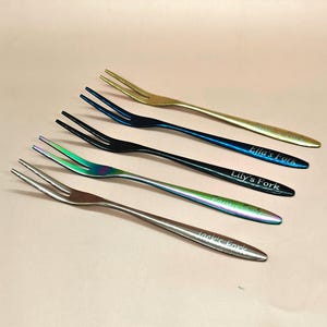 Könnte beinhalten: Fünf dekorative Gabeln in Gold, Blau, Schwarz, schillernd und Silber. Jede Gabel ist mit einem Namen graviert: "Rose's Fork", "Ella's Fork", "Lily's Fork", "Kamila's Fork" und "Jack's Fork".