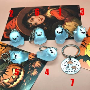 May include: A collection of Halloween-themed keychains featuring translucent ghost designs. Some keychains have smiling faces, while one has a circular tag with the text "You're my Boo" and a ghost illustration. The background includes a pumpkin and a witch illustration.