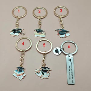 May include: A selection of graduation keyrings. Each keyring has a gold-coloured ring and chain, with charms showing graduation caps, diplomas, and bouquets. One keyring has the text "Graduation is not the end. It's the beginning."