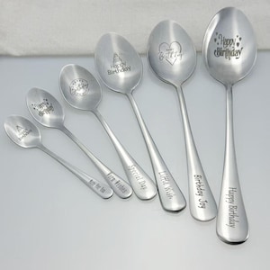 Puede incluir: Seis cucharas de acero inoxidable con mensajes grabados. Las cucharas presentan frases como "Feliz Cumpleaños" y "Pequeño Deseo". Los cuencos de las cucharas muestran diseños como un pastel y un corazón. Medidas en centímetros.