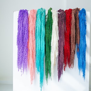 May include: A display of artificial hanging flowers in a variety of colours, including purple, pink, turquoise, green, white, burgundy, red, brown, and blue. The faux flowers are suspended against a white backdrop, highlighting their diverse colours and textures.