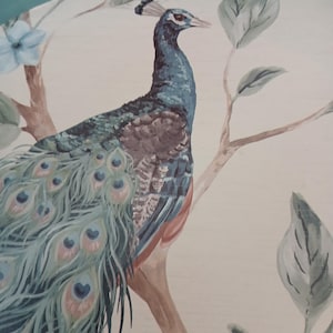 Puede incluir: Pintura detallada de un pavo real posado en una rama, con plumas azules, turquesas y marrones. La obra de arte incluye hojas verdes suaves y una flor azul claro, sobre un fondo color crema.