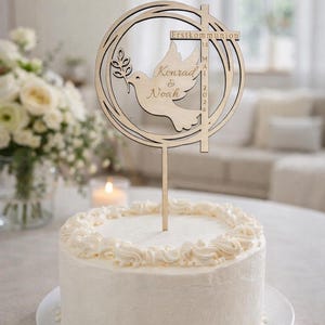 Puede incluir: Una tarta blanca glaseada con un adorno de pastel de madera. El adorno presenta una paloma con una rama de olivo, los nombres "Konrad & Noah" y el texto "Erstkommunion" con la fecha "14 de mayo de 2026".