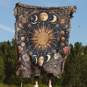 May include: A tapestry throw blanket with a dark blue background featuring a gold sun and moon design with floral accents.