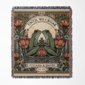 May include: A woven tapestry with a vintage-inspired design featuring two green frogs facing each other. The tapestry has a floral border with red and orange flowers. The text "Until We Croak" is written in a decorative font above the frogs. Below the frogs, the text "Juliana & David Est. 2021" is written in a smaller font.