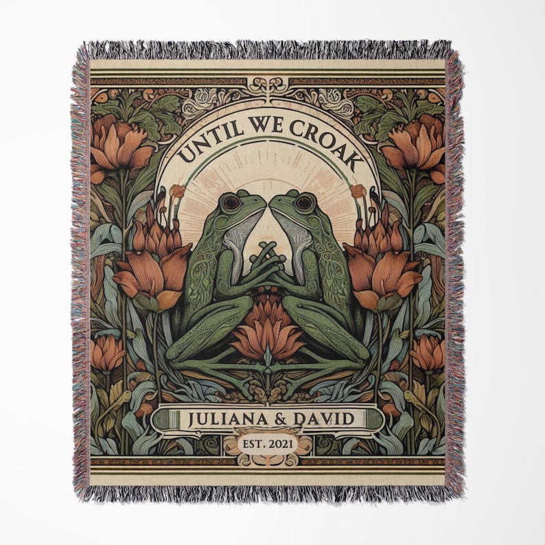 May include: A woven tapestry with a vintage-inspired design featuring two green frogs facing each other. The tapestry has a floral border with red and orange flowers. The text "Until We Croak" is written in a decorative font above the frogs. Below the frogs, the text "Juliana & David Est. 2021" is written in a smaller font.