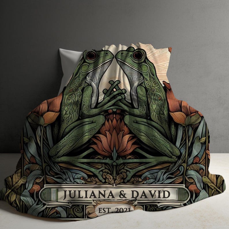 May include: A green and brown throw blanket with a floral design and two frogs facing each other. The blanket has the text "Juliana & David EST 2021" in a banner at the bottom.