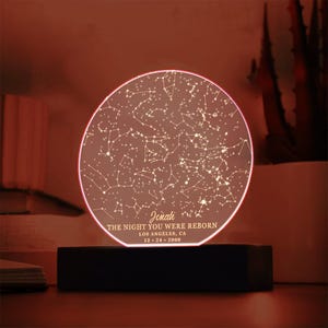 Puede incluir: Un mapa de estrellas redondo, blanco e iluminado con una base negra. El mapa muestra las constelaciones visibles el 24 de diciembre de 2000 en Los &Aacute;ngeles, California. El texto "Jonah, The night you were reborn" est&aacute; impreso debajo del mapa.