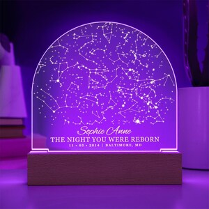 Puede incluir: Una luz nocturna morada con una base de madera. La luz presenta un mapa de constelaciones con el texto "Sophie Anne THE NIGHT YOU WERE REBORN 11.05.2014 | BALTIMORE, MD"