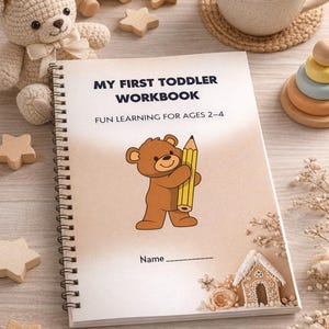 May include: A spiral-bound workbook titled "MY FIRST TODDLER WORKBOOK" with the subtitle "FUN LEARNING FOR AGES 2-4." The cover features a brown bear holding a yellow pencil. Additional wooden toys and a cup of tea are in the background.