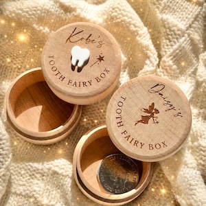 May include: Two round wooden boxes with lids. One lid features the engraved text Kobe's Tooth Fairy Box and a small white tooth icon. The other lid features the engraved text Daisy's Tooth Fairy Box and a fairy silhouette. A silver coin sits inside.