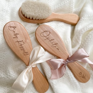 May include: A set of wooden baby brushes. Two brushes are engraved with names and tied with satin ribbons. One brush is engraved with the name "Baby Russell", the other with "Ophelia". The set includes a brush with soft bristles.